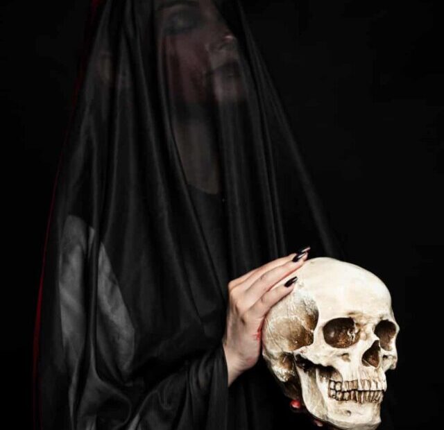 mulher veste véu preto e segura um crânio