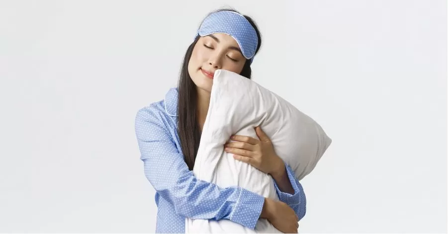 mulher de pijamas abraçada com um travesseiro pronta par a ir dormir