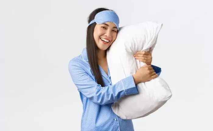 Mulher de pijamas depois de fazer a rotina eficaz de skincare abraçando um travesseiro se sentindo plena