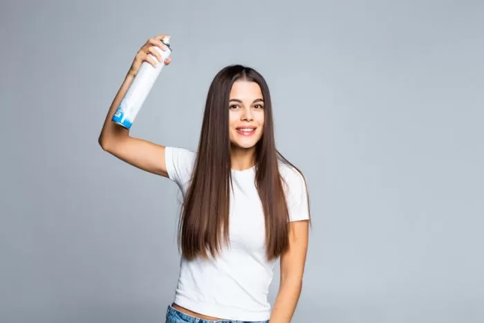 mulher com uma lata de spray na mão para retocar a raiz dos cabelos em casa.