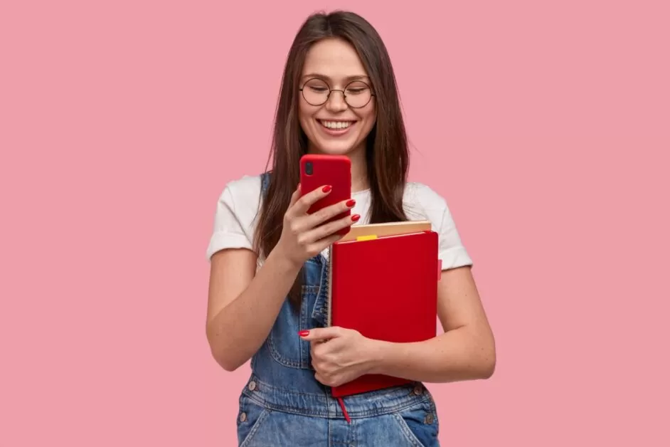 Jovem abraçada com livros enquanto assiste a um vídeo no TikTok pelo celular